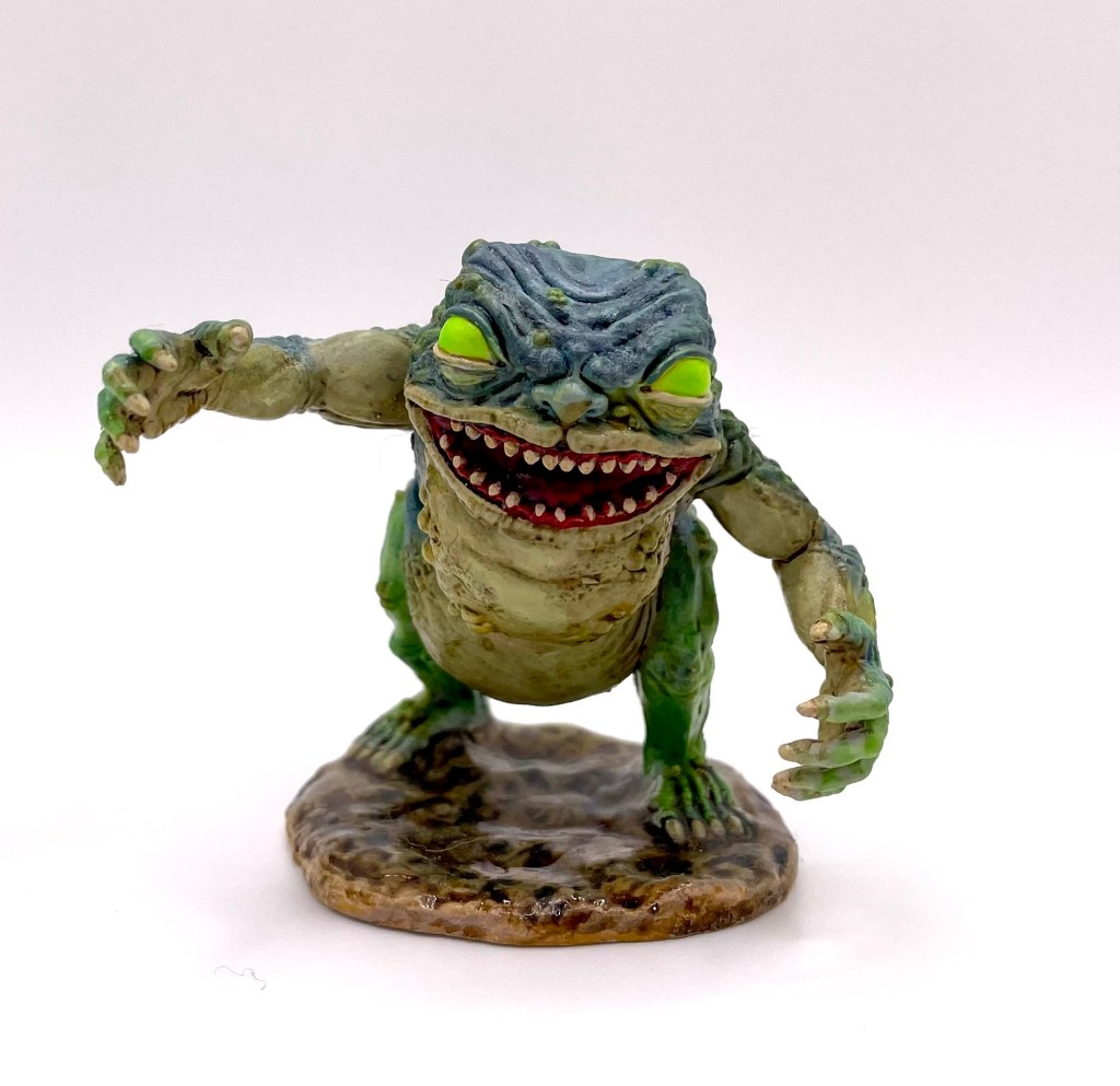 A banderhob. Dull blue, tan, and green body. Large mouth with bloody teeth. Acid green eyes. 